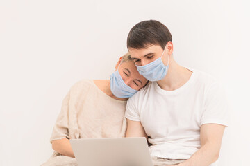 A family in medical masks look at a laptop. The old mother and young son. The concept of self-isolation at home due to the virus pandemic. Spending time during quarantine.