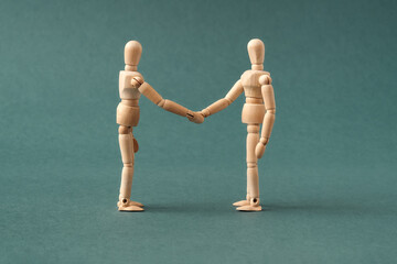 Two wooden figures shaking hands on blue background, friendship or agreement concept