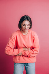Woman wearing casual sweater on background suffering stomach ache with painful grimace, feeling sudden period cramps, gynecology concept