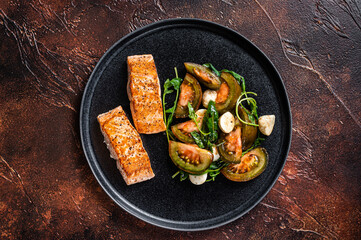 Grilled Salmon Fillet Steaks with arugula and tomato salad on a plate. Dark background. Top view