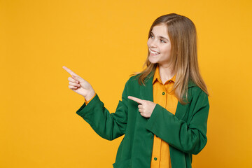 Little blonde kid girl 12-13 years old in casual clothes green shirt point index finger aside on copy space mock up isolated on yellow orange background children studio. Childhood lifestyle concept