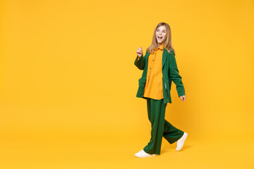 Full length little blonde kid happy girl 12-13 years old wearing casual clothes walking smiling look aside isolated on yellow orange background children studio portrait. Childhood lifestyle concept