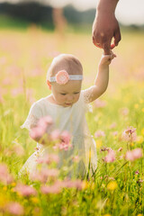 smiling little girl in white dress is walking in field with wild flowers. child having fun with...