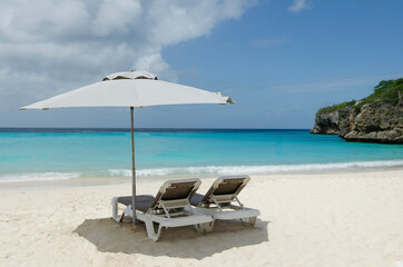 Two rest chairs under parasol in tropical Caribbean beach with turquoise water.  Summer holiday and vacation concept