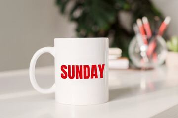 Coffee mug with text SUNDAY in workplace background.