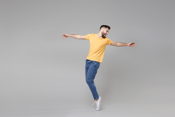 Full length of young bearded attractive handsome relaxed man 20s in casual yellow basic t-shirt with outstretched hand leaning over looking aside isolated on grey color background studio portrait.