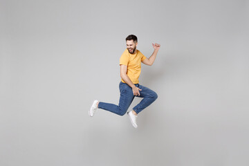 Fototapeta na wymiar Full length of young bearded student smiling happy overjoyed man 20s in yellow basic t-shirt jump high playing guitar gesture flying outstretched hands isolated on grey background studio portrait