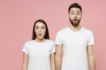 Young shocked surprised happy couple two friends bearded man brunette woman in white basic blank print design t-shirts keep mouth open say wow isolated on pastel pink color background studio portrait.