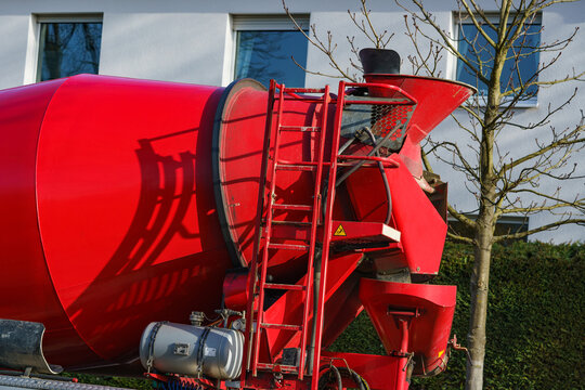 A fragment of a red concrete mixer on the car. Against the background of the white house.