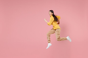 Fototapeta na wymiar Full length side view of young smiling brunette excited overjoyed attractive latin woman 20s in yellow shirt running fast jumping high hurrying isolated on pastel pink background studio portrait