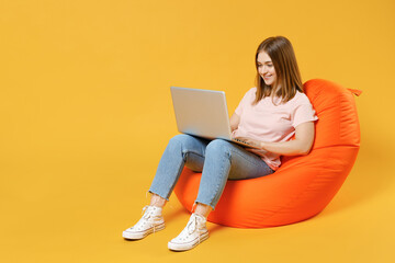 Full length of young student woman 20s in basic pastel pink t-shirt, jeans sitting in orange bean...