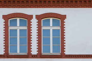 White wall of the building with two windows on the left side. The windows are framed with red bricks.