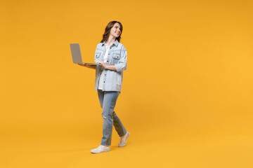 Full length of young freelancer copywriter smiling student happy woman in denim shirt white t-shirt hold laptop computer working online look aside back isolated on yellow background studio portrait.