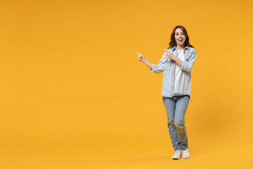 Fototapeta na wymiar Full length of young smiling friendly fun student happy woman 20s in denim shirt white t-shirt pointing index finger aside on worspace area mock up isolated on yellow color background studio portrait