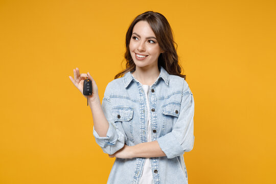 Young smiling dreamful pensive wistful happy rich brunette woman 20s wearing stylish denim shirt white t-shirt holding in hands car keys look aside isolated on yellow color background studio portrait.