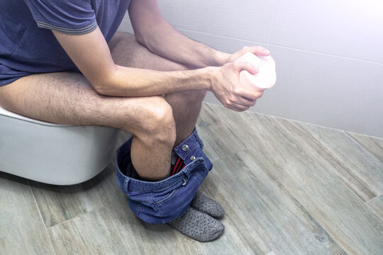 Close up of Man sitting in toilet feeling unhappy and squeezes a toilet paper roll. Diarrhea constipation, health concept