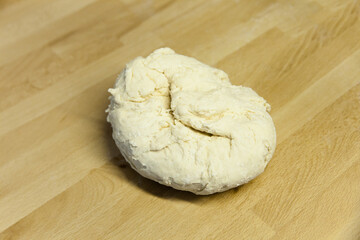 Freshly kneaded hard unripened wheat dough on a wooden table. Preparation of dough for manti, dumplings, khinkali. 