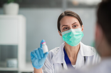 A young medical woman holds a bottle of vaccine in her hands and shows it.