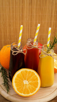 Home made lemonade in little bottles. Multicolored juices and fruits on wooden background. Vertical photo