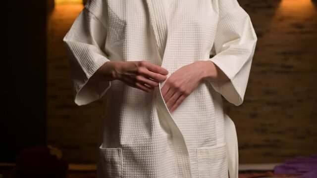 the woman unties the belt of the robe and does not fully open it. Mysterious young woman stripping