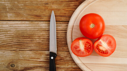 Slice Tomato on a Wooden Cutting Board. Knife and tomatoes on a wooden background. Cooking and kitchen concept