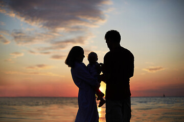 The silhouette of the family mom, dad child against the background of the sunset and the sea