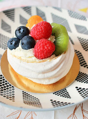 Mini pavlova meringue with cream, raspberries, blueberries and kiwi, served on a golden tray and a black and white plate