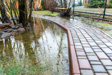 Garden bushes, tree and green grass lawn covered with water due to snow melting thaw and flash high...