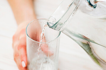 A female is pouring fresh, clear water from a jug into a glass. Health and diet concept. Clean...