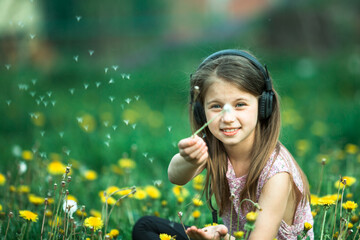 Little funny girl in headphones in the green field.