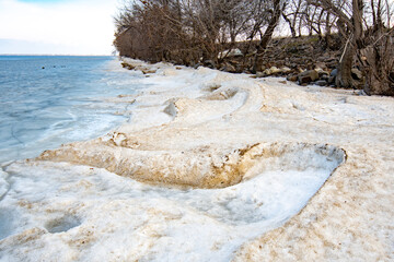 Dirty snowdrifts on the shore near the dam. Against the background of trees