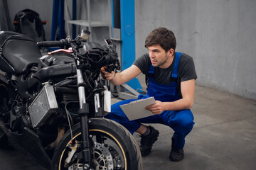 Fototapeta na wymiar A repairer inspects a motorcycle. He is wearing a blue overalls