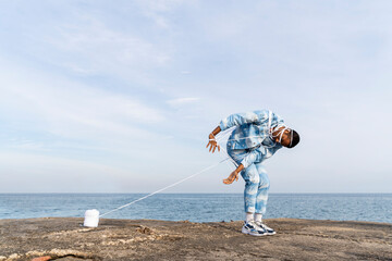 Young man trapped in rope escaping while standing against sky