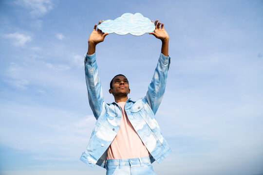 Man holding cloud cut out while standing against sky