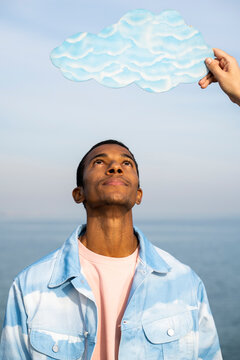 Man standing and looking at male hand holding cloud cut out against sky