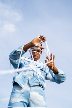 Trapped young man removing rope while standing against sky