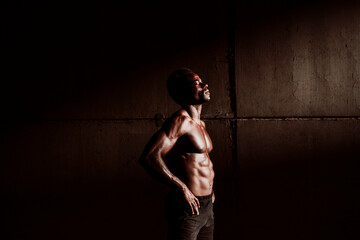 Contemplating sportsman with bare chested hand on hip standing by gray wall during sunset