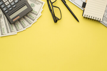 Photo overhead of calculator money pen glasses notebook and keyboard isolated on the yellow...