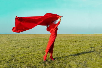 Senior woman holding red fabric while standing on grass against blue sky