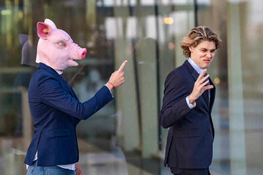 Young male professional irritated by arguing with colleague in pig mask while walking by glass wall
