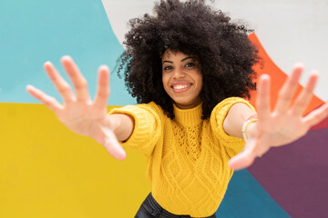 Smiling woman stretching hands while standing against colorful wall