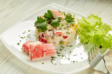 Appetizing salad from crab sticks with rice and vegetables on light wooden table.