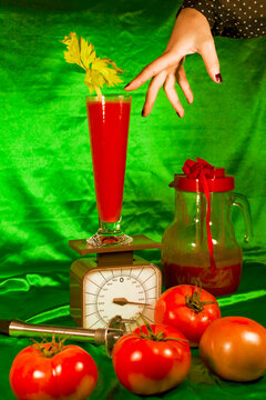 Hand by glass of juice on weight scale around fresh tomatoes