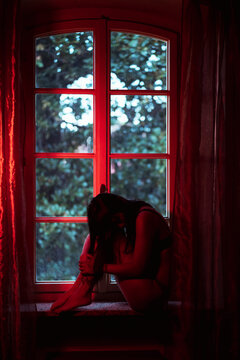 Woman sitting with hugging knees at window sill