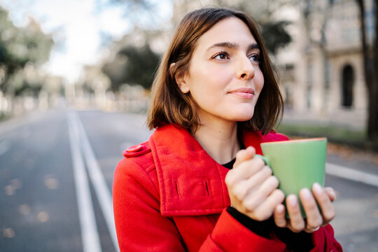 Young woman with coffee cup day dreaming while standing on street