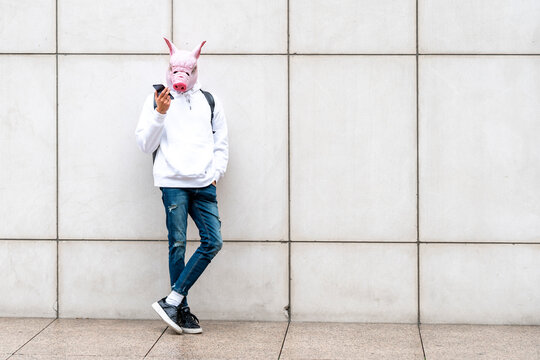 Man with pig mask sending voicemail on smart phone against wall