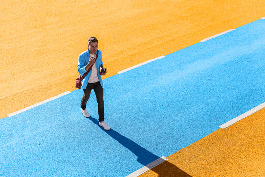 Young man talking through smart phone while walking on yellow and blue street during sunny day