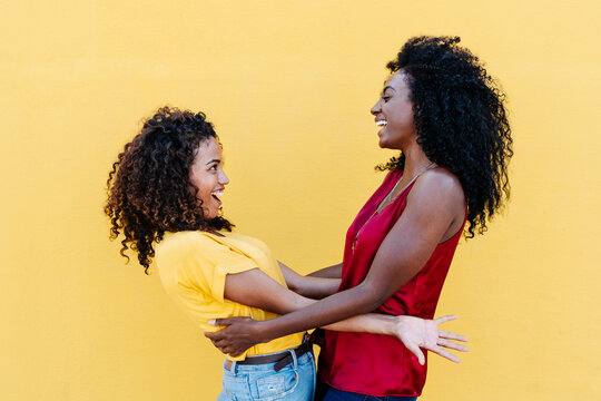 Lesbian couple laughing while looking at each other by yellow wall
