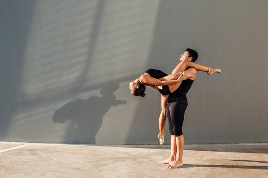 Young man helps flexible woman do dance pose against wall