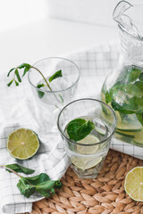 Detox water with lime fruit and mint leaves in jar and glasses